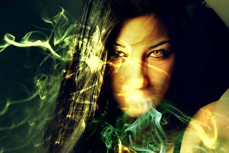 A red-eyed woman with dark hair has magic weaves in front of her face.