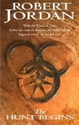 The Hunt Begins paperback, June 2004 edition from Atom. The cover has the snake-wheel symbol partially submerged by sand.